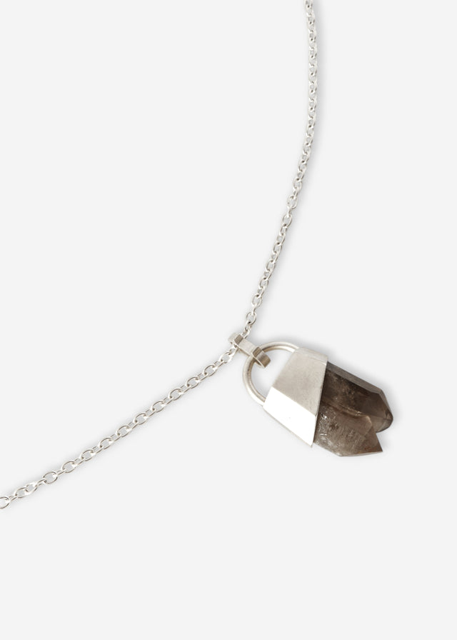Raw brown quartz point in a faceted silver cap on a slim silver cable chain, pale grey studio backdrop — STRUGA