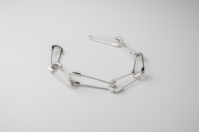 Polished silver bracelet of interlocking safety-pin links, lit on a pale grey studio backdrop — STRUGA