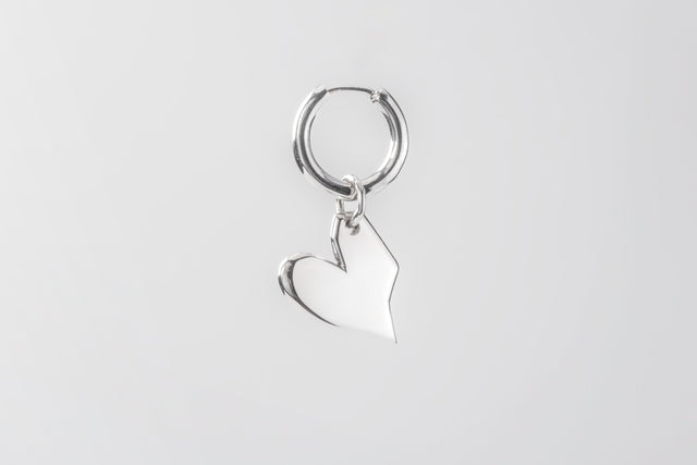 Silver huggie hoop earring with a smooth solid heart charm, single piece on a plain light grey studio background — STRUGA