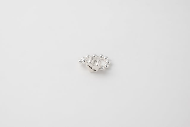 Silver bead ring seen from the side, small heart set among the beads, pale ground — STRUGA