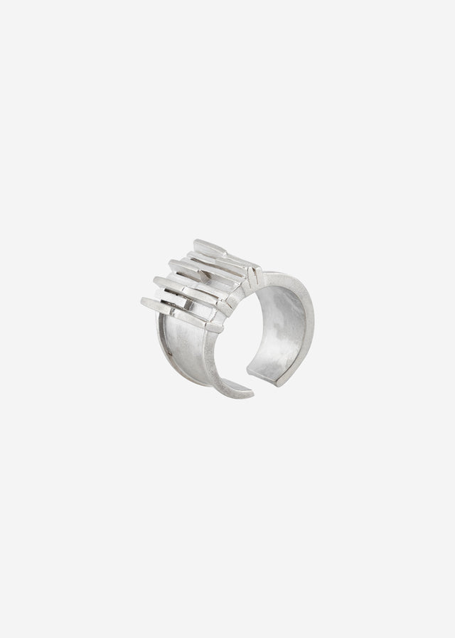 Matte silver ear cuff: wide open band crossed by flat bars of uneven length, light grey studio backdrop — STRUGA