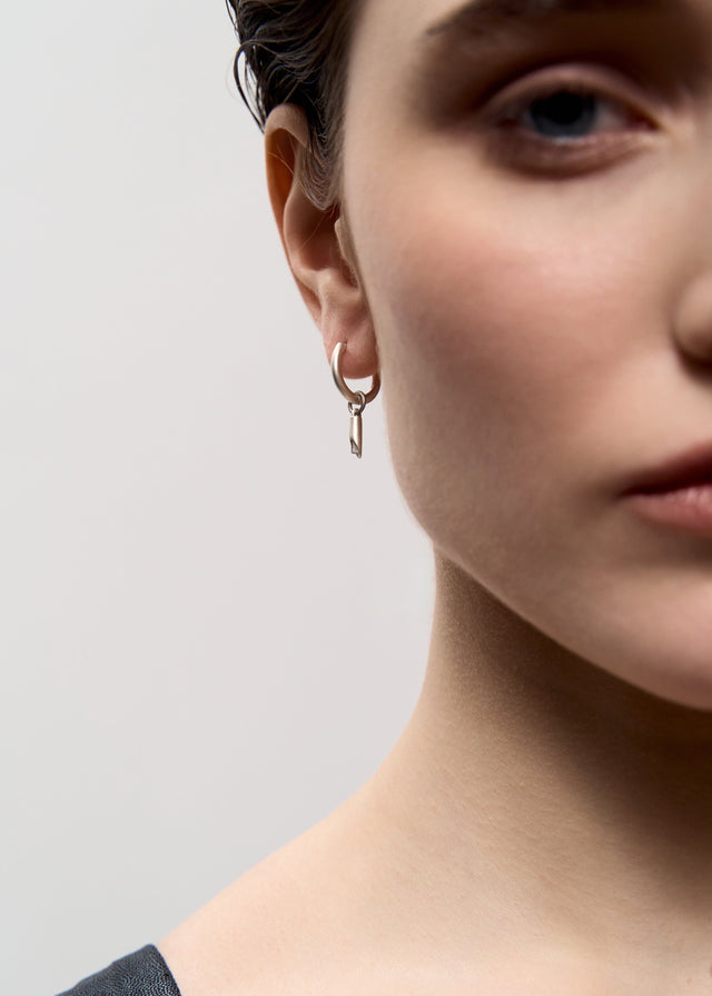 Small silver hoop with a hanging bar on the ear, grey studio ground — STRUGA