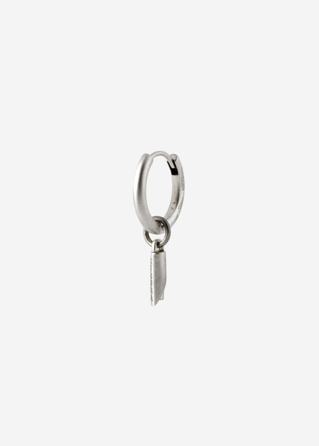 Single silver huggie hoop with a small rolled cylinder charm, turned three-quarter on a pale grey studio ground — STRUGA