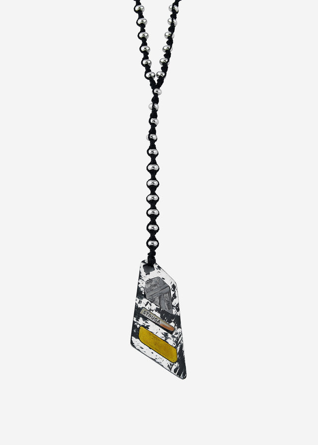 Angular black-and-white tag pendant, etched grey and yellow inlays, black cord with polished beads, pale backdrop — STRUGA