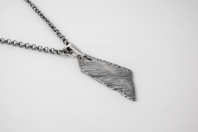 Dark textured silver shard pendant on a heavy ball chain, pale ground — STRUGA