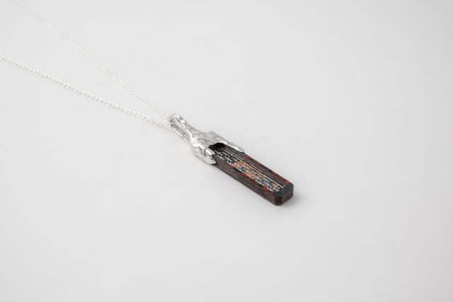Bar pendant on white chain: dark layered slab, rust-red streaks, honeycomb inlay, molten white cap, grey studio — STRUGA