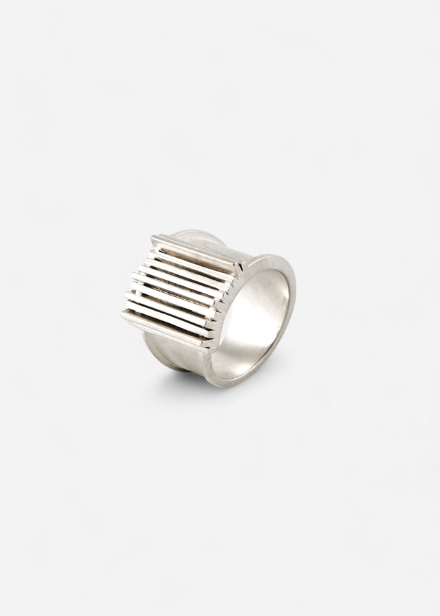 Wide band ring with a ribbed rectangular top plate, cool white metal, mirror highlights, pale grey studio backdrop — STRUGA