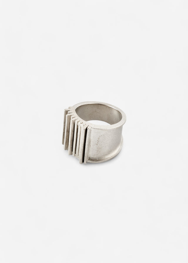 Wide silver Brutalism ring at three-quarters, ribbed bars along one side, pale ground — STRUGA