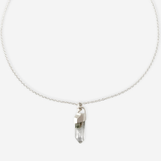 Slim silver cable chain with a raw clear quartz point in a faceted silver cap, pale grey studio backdrop — STRUGA