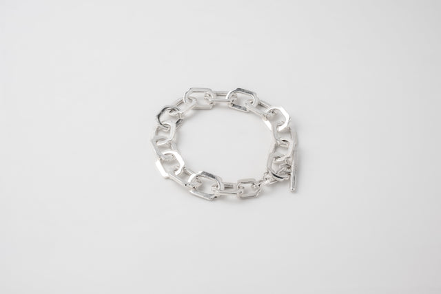Polished silver bracelet of chunky rectangular links with a toggle bar clasp, on pale grey seamless — STRUGA