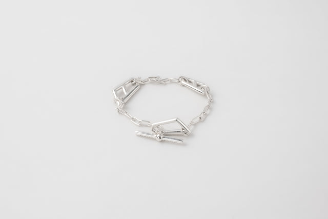 Polished silver bracelet laid in an open ring, flat angular links and a toggle bar clasp, pale grey studio backdrop — STRUGA