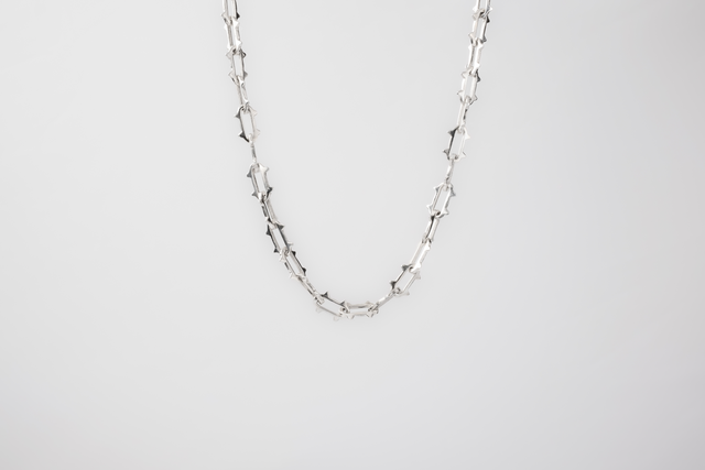 Thorn chain in light 925 silver: elongated links with side spikes, laid in an arc on a white background