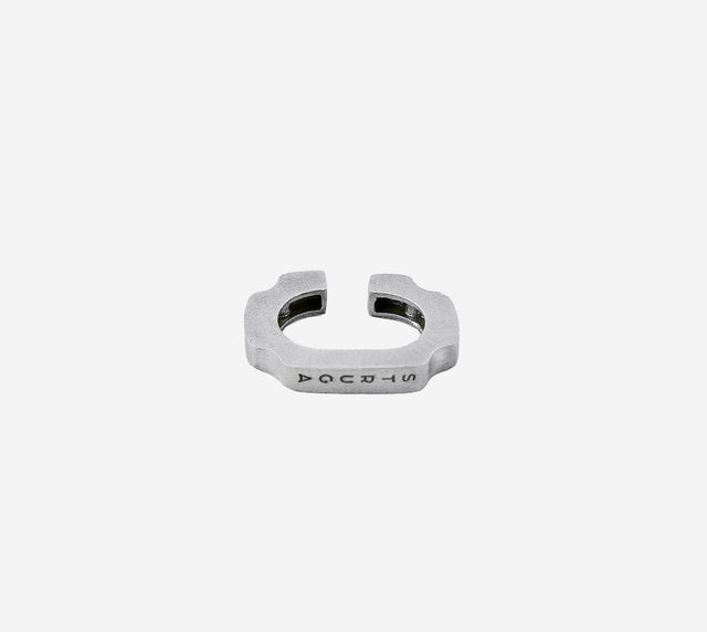 Heavy open band in matte silver with notched shoulders and engraved STRUGA mark on pale grey studio ground — STRUGA