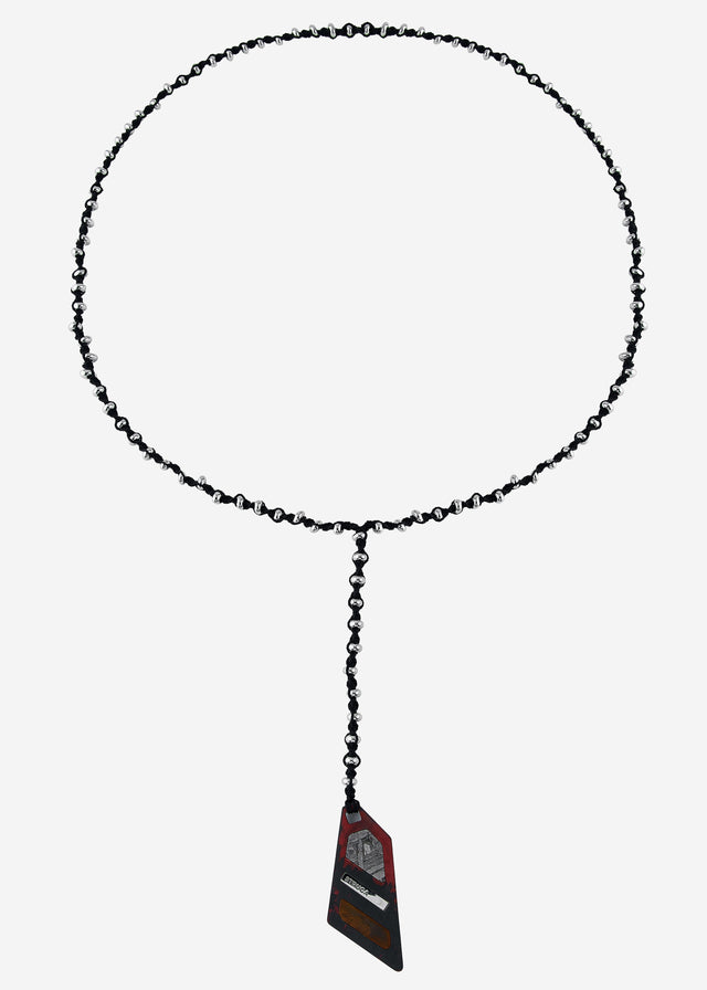 Silver-beaded black cord necklace coiled flat on grey, red-black wedge pendant set with a grey meteorite slice — STRUGA