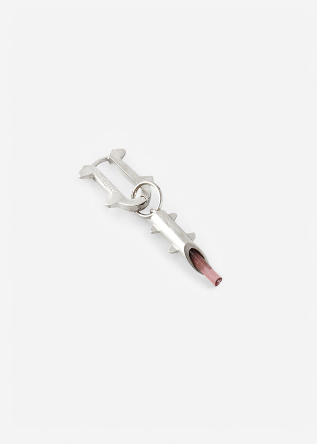 Silver thorn-frame mono earring with a translucent pink stone tip, laid flat on pale grey — STRUGA