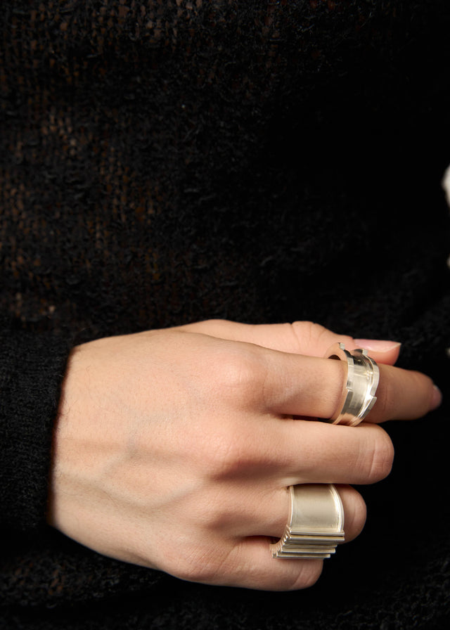 Two wide silver Brutalism rings on a hand against a black knit sleeve — STRUGA