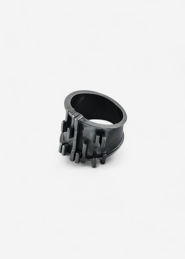 Blackened silver Brutalism V.3 ring, stepped relief across the face, pale ground — STRUGA