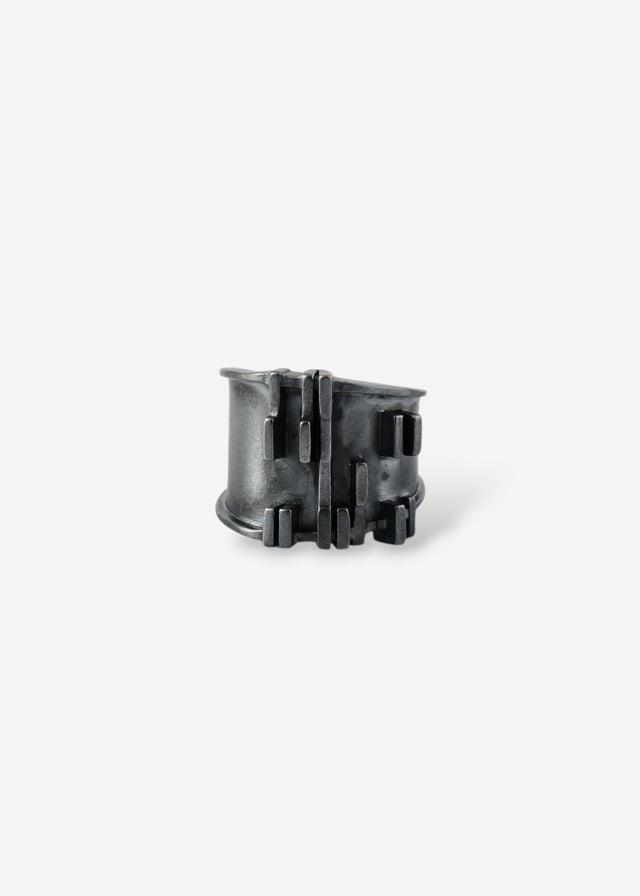 Blackened silver Brutalism V.3 ring head-on, raised bars across a dark band, pale ground — STRUGA